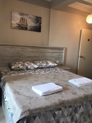A neatly made bed with a patterned bedspread, a pillow with a geometric design, and a painting of a sailboat on the wall. - Su Residence (Trabzon)