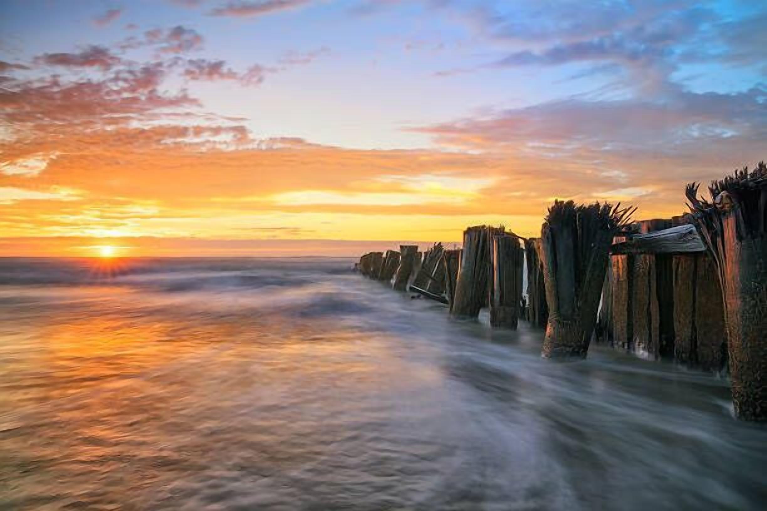 A sunset over a calm sea with wooden structures extending into the water.