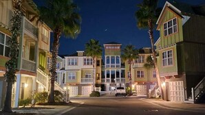 A row of multi-story buildings with balconies, a central building with a prominent entrance, and palm trees.