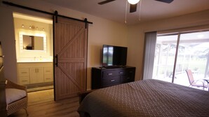 Un dormitorio con cama, televisor, puerta corredera al baño y vistas al exterior.