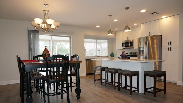 Una cocina moderna con comedor, que presenta una araña, luces colgantes, una isla central con taburetes y electrodomésticos de acero inoxidable.