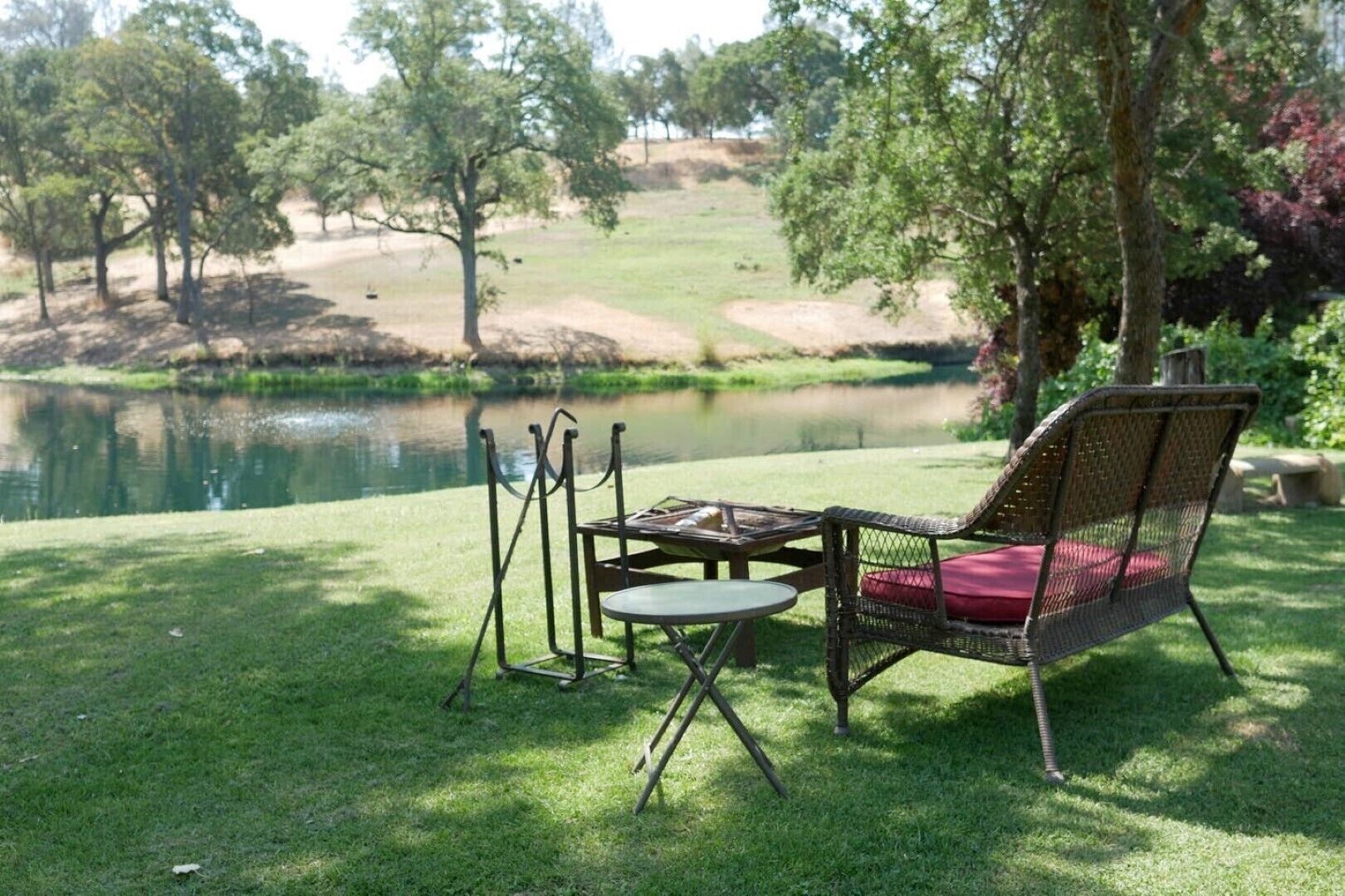 A grassy area with a pond, a chair, and a table.