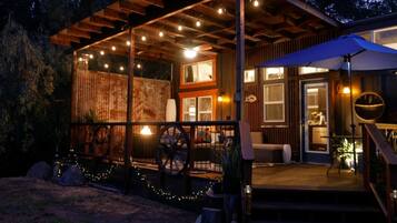 A wooden cabin with a covered porch, string lights, and a large umbrella.