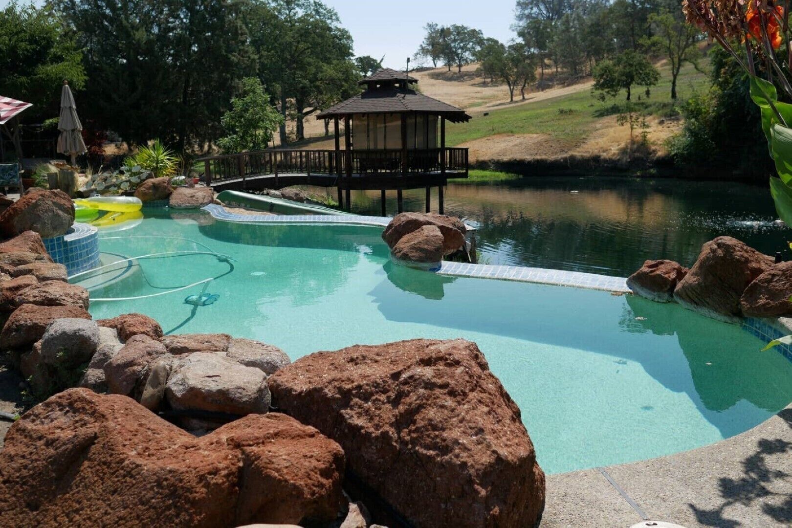 A swimming pool with rocks, a wooden deck, and a gazebo.
