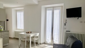 Una habitación moderna y bien iluminada con una mesa de comedor, sillas, un sofá y un televisor de pantalla plana montado en la pared.