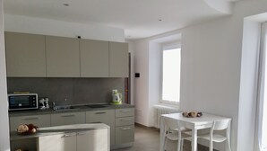 Una cocina moderna con área de comedor, que incluye una mesa y sillas blancas, horno empotrado y ventana que proporciona luz natural.