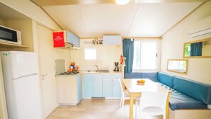 Cocina compacta equipada con microondas, refrigerador, lavaplatos y estufa. Hay una mesa de comedor con sillas y un sofá azul.