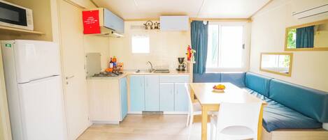 Cocina compacta equipada con microondas, refrigerador, lavaplatos y estufa. Hay una mesa de comedor con sillas y un sofá azul.