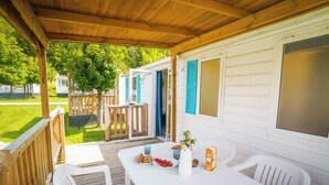 Un espacio al aire libre techado con una mesa blanca dispuesta con comida, rodeada de sillas de plástico blancas.