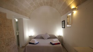 A bedroom with a stone wall, a bed with towels, a nightstand, and a dresser. - Authentic Trullo & Villa with Pool – Perfect for Families & Groups (Ceglie Messapica)