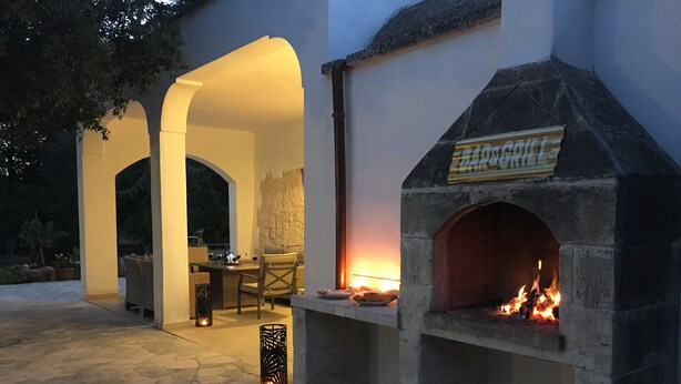 An outdoor patio with a stone fireplace, a table with chairs, and a sign reading "BAR&GRILL". - Authentic Trullo & Villa with Pool – Perfect for Families & Groups (Ceglie Messapica)