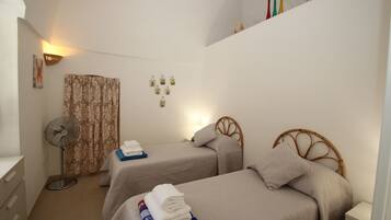 Two single beds with wooden headboards and beige bedspreads, a bedside table, and a wall-mounted fan.