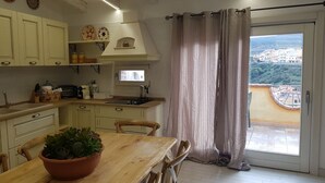 Una cocina con una mesa de comedor, sillas, una planta en maceta y vistas a un pueblo a través de una ventana.