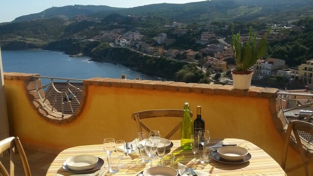 Una mesa de comedor en un balcón con vistas a un pueblo costero, el mar y colinas.