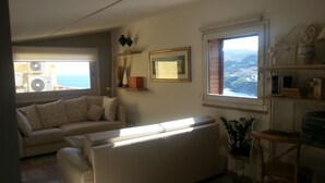Una sala de estar con un sofá, una silla, una mesita y una ventana con vista al mar.