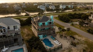 Una propiedad frente al mar con varios pisos, piscina, mobiliario exterior y vista al agua y casas circundantes.