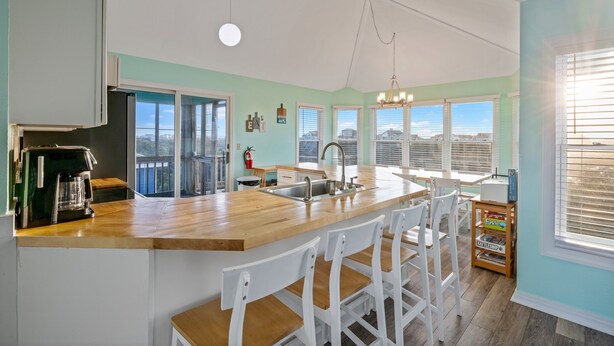 Una cocina con encimera de madera, taburetes de bar blancos, una cafetera y vistas de la ciudad a través de amplias ventanas.