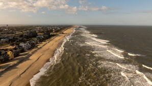 Vista costera con playa, océano y una hilera de casas a lo largo de la orilla.