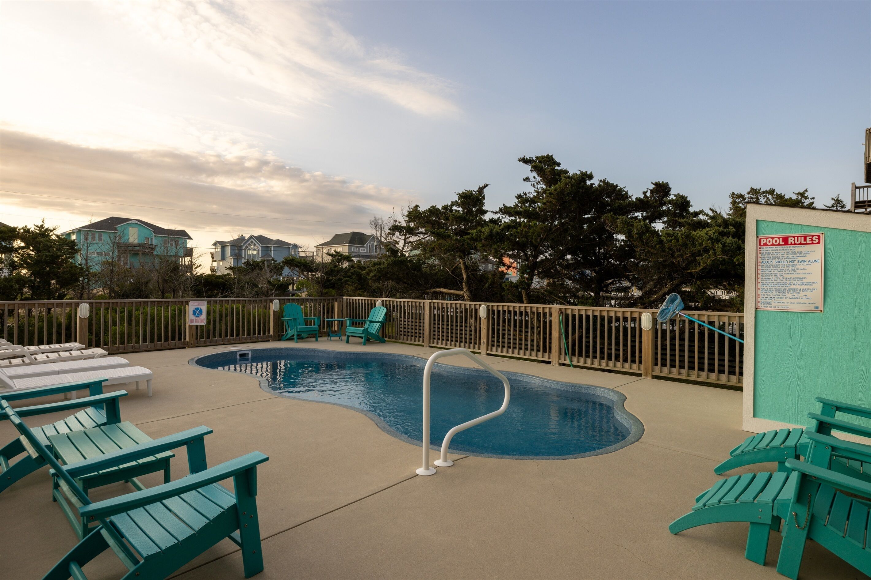 A swimming pool with a pool ladder, lounge chairs, and a 'Pool Rules' sign.