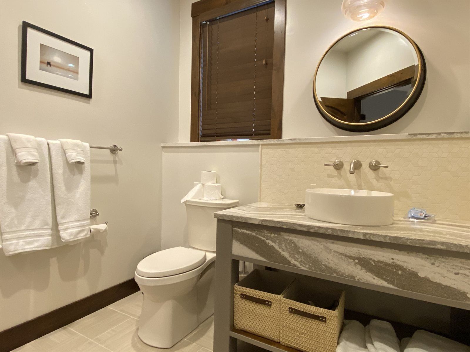 A bathroom with a toilet, a sink with a mirror, and a framed picture on the wall.