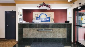 Un mostrador de recepción con el logotipo de Days Inn, una puerta negra con la leyenda "Oficina" y una cámara de seguridad sobre el mostrador.