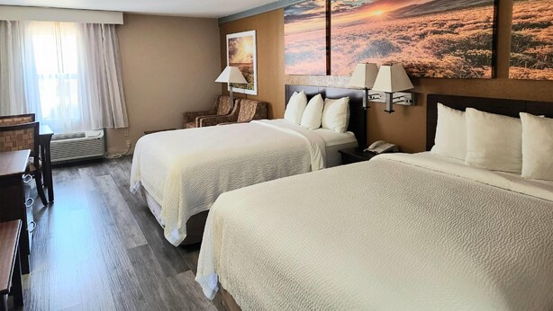 Habitación de hotel con dos camas, un escritorio, una silla, una lámpara y un cuadro grande en la pared.