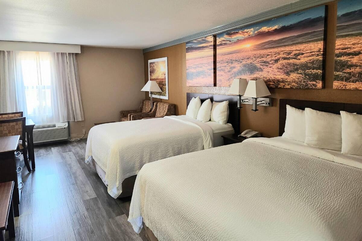 A hotel room with two beds, a desk, a chair, a lamp, and a large painting on the wall.