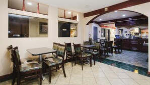 Un restaurante con sillas y mesas de madera, una zona de cocina y un suelo de baldosas.