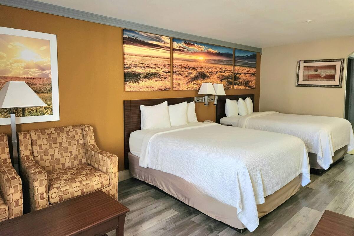 A hotel room with two beds, a sofa, a lamp, and a painting of a sunset.