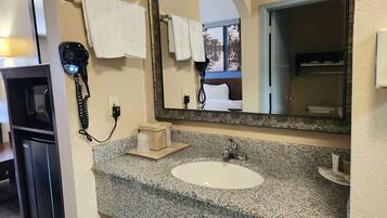 A hotel bathroom with a granite countertop sink, a large mirror, a hairdryer, and a towel rack.