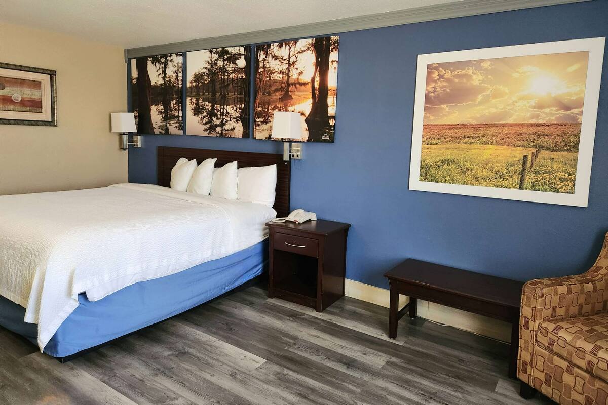 A hotel room with a large bed, a nightstand, a chair, and two wall-mounted lamps.