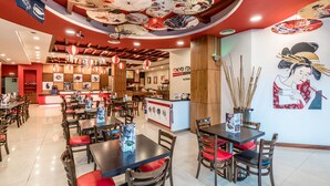 Un interior de restaurante con mesas de madera y sillas rojas, una barra de sushi y decoraciones tradicionales japonesas.