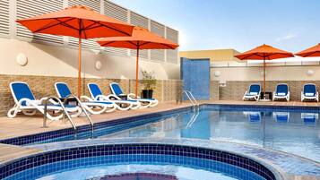 A swimming pool with blue tiled edges, lounge chairs, and orange umbrellas.