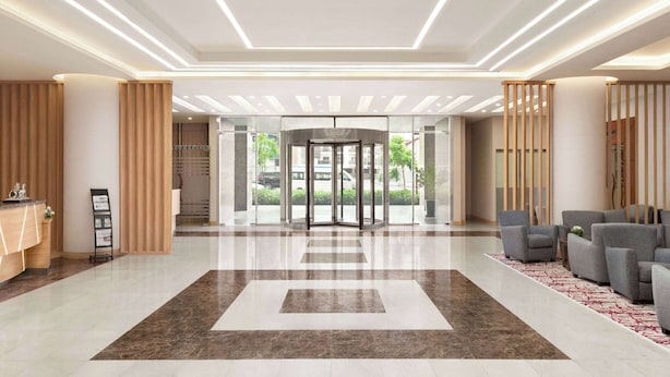 Un moderno vestíbulo de hotel con mostrador de recepción, puerta giratoria y zona de estar con sofás.