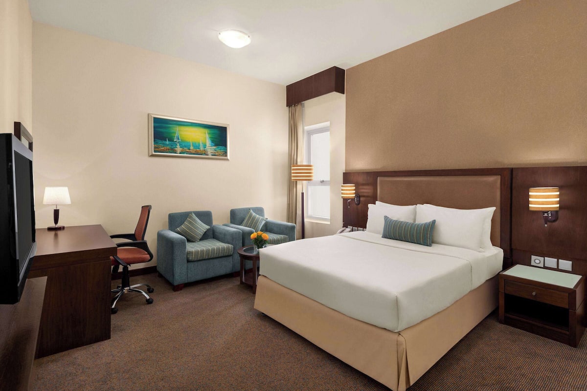 A hotel room with a large bed, a desk, a chair, and a sofa.