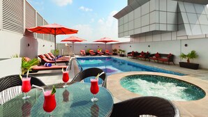Un área de piscina en la azotea con sillones, sombrillas rojas y un jacuzzi.