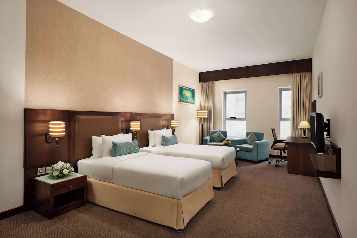 A hotel room with two beds, a desk, a chair, and a TV.