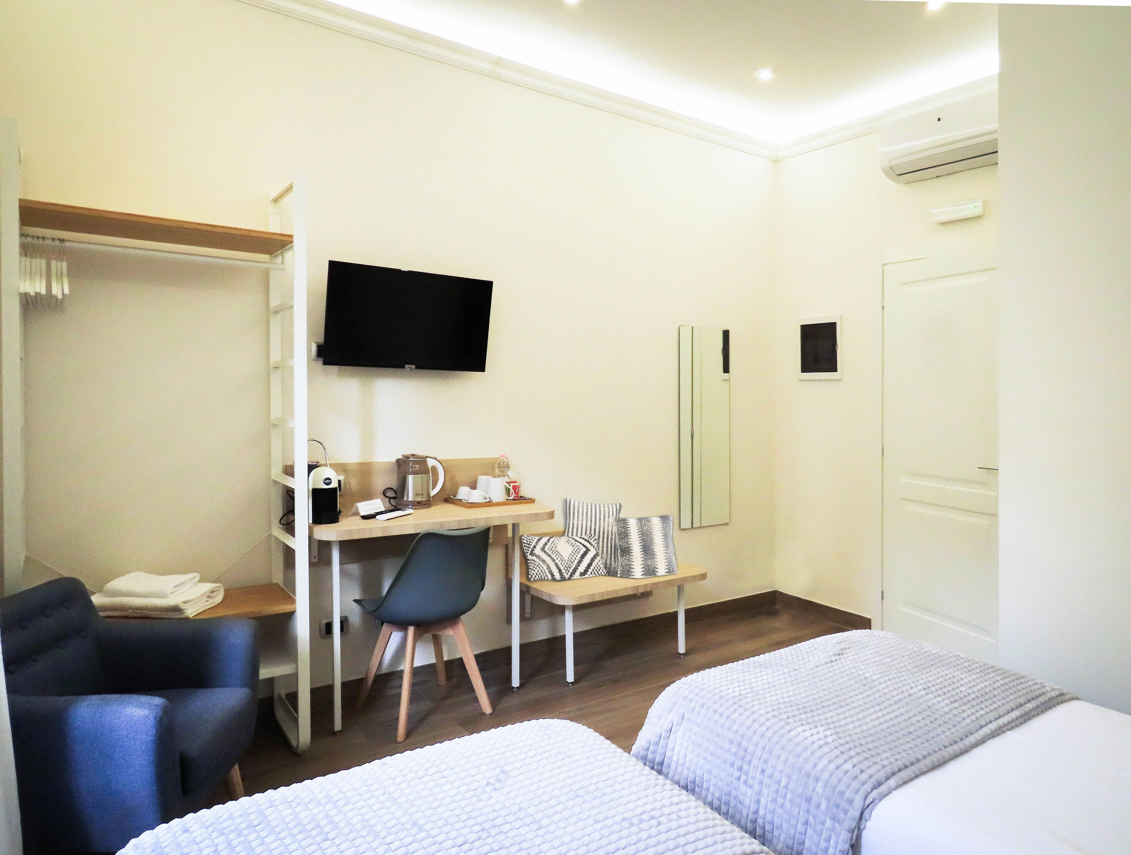 A hotel room with a bed, a desk with a chair, a television, and a wardrobe.