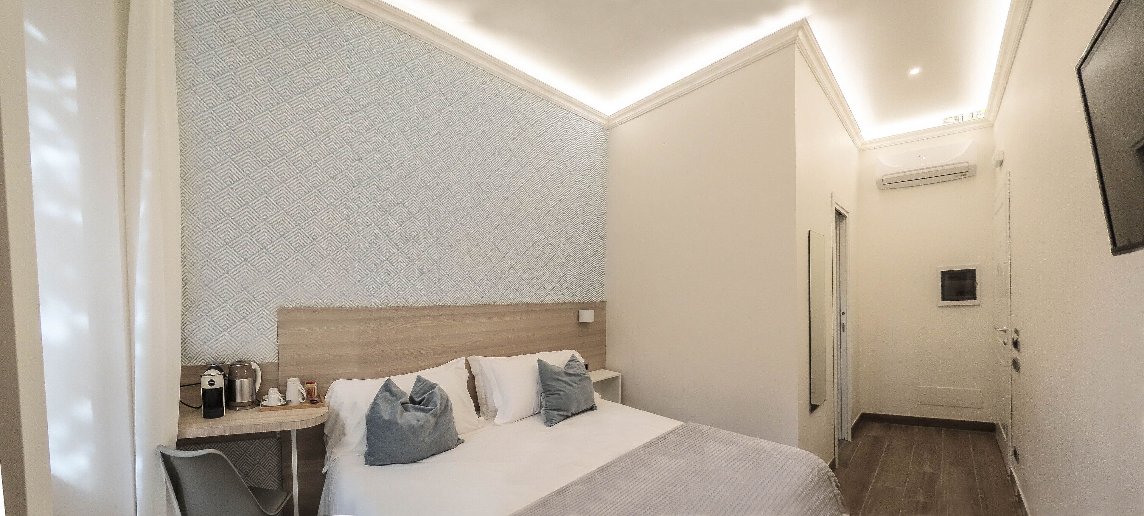 Habitación de hotel con cama, mesita de noche y televisor montado en la pared.