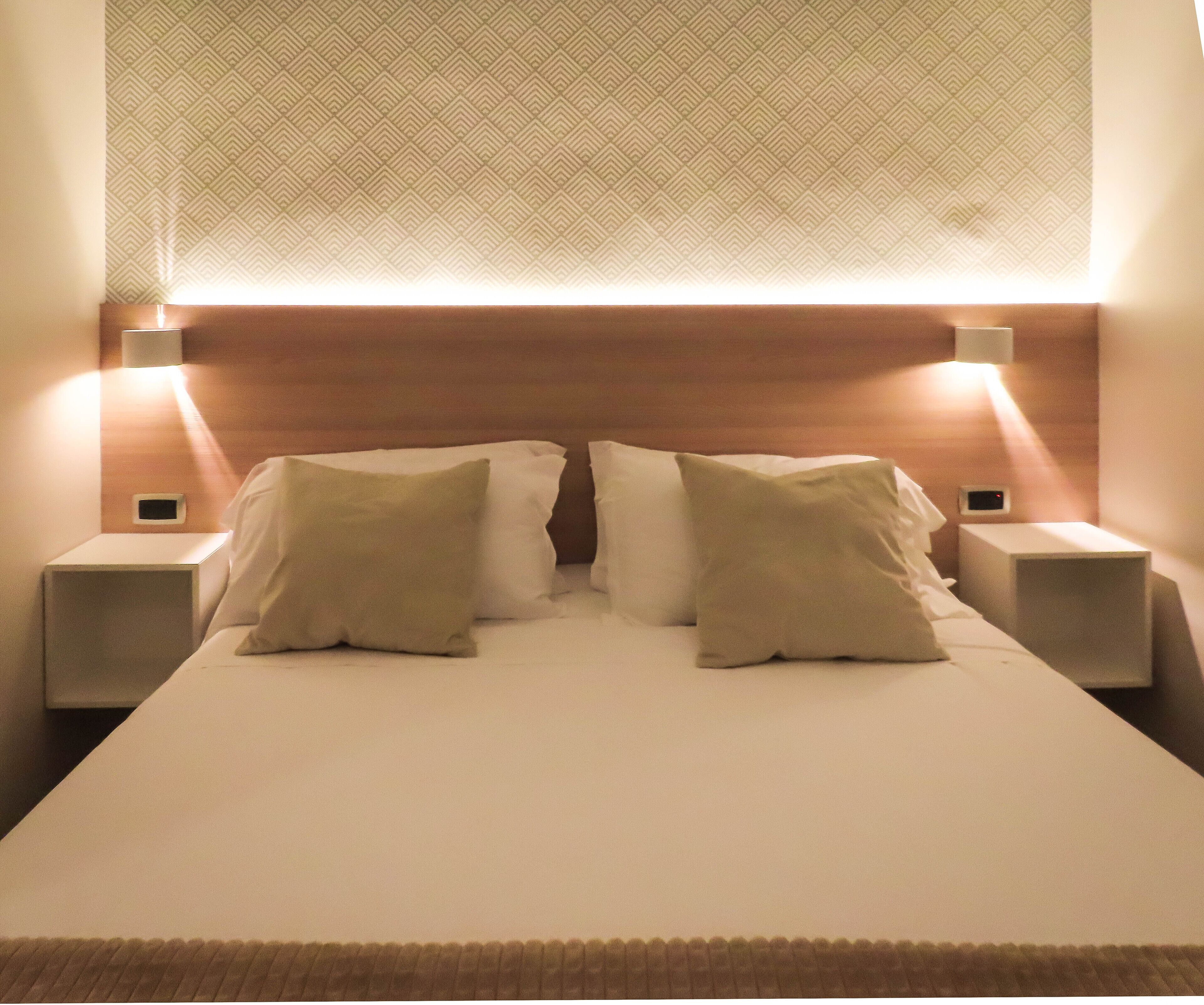 A neatly made bed with two pillows, a headboard with a geometric pattern, and bedside lamps on either side.