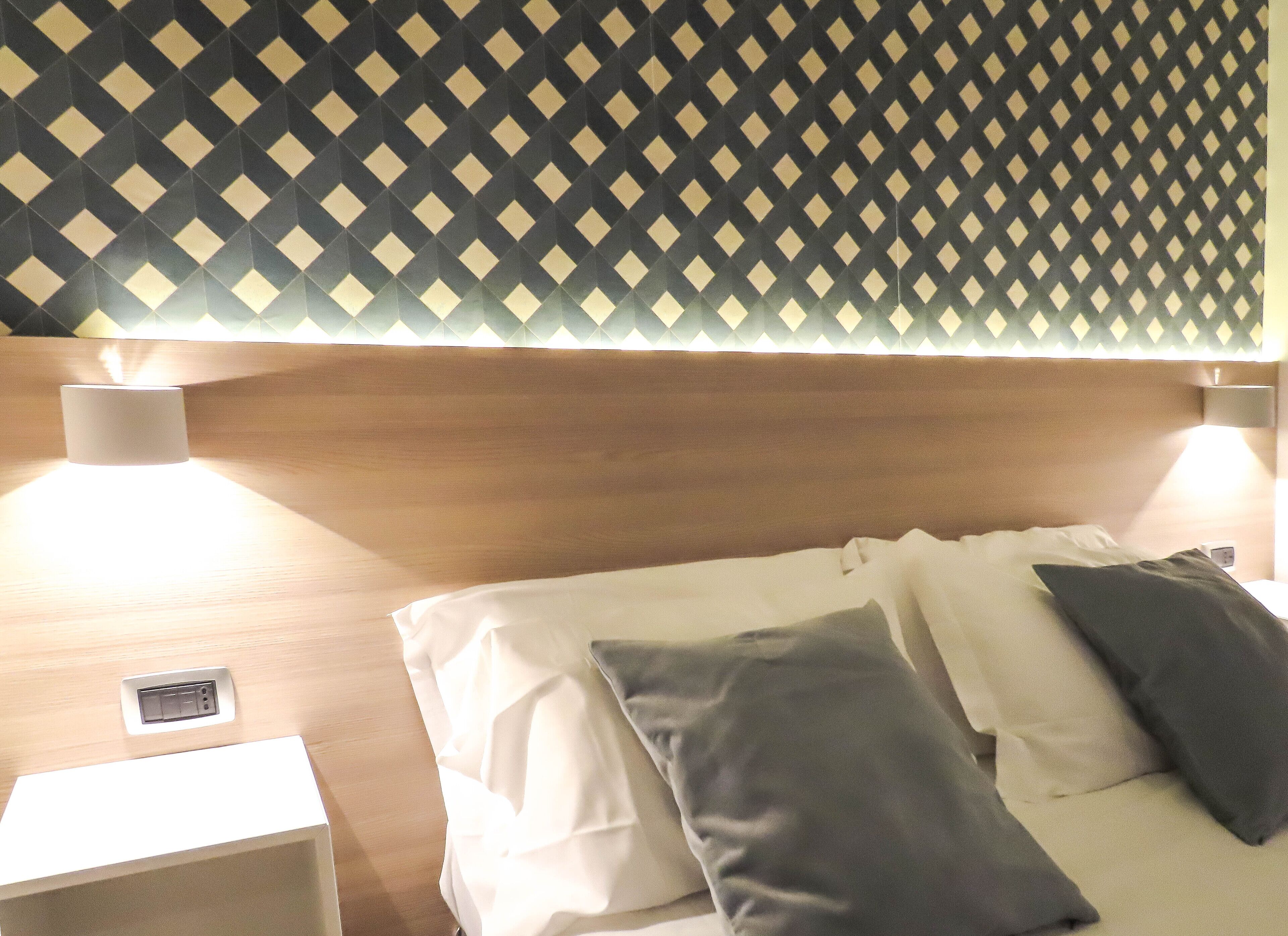 A hotel room with a patterned wall, a wooden headboard, and a bedside table with a lamp.