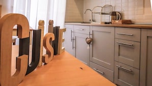 A kitchen with a wooden table displaying large letters spelling "CUISE," a heart-shaped decoration on a cabinet door, and a kitchen sink with a faucet. - My Maison 109 (Rome)