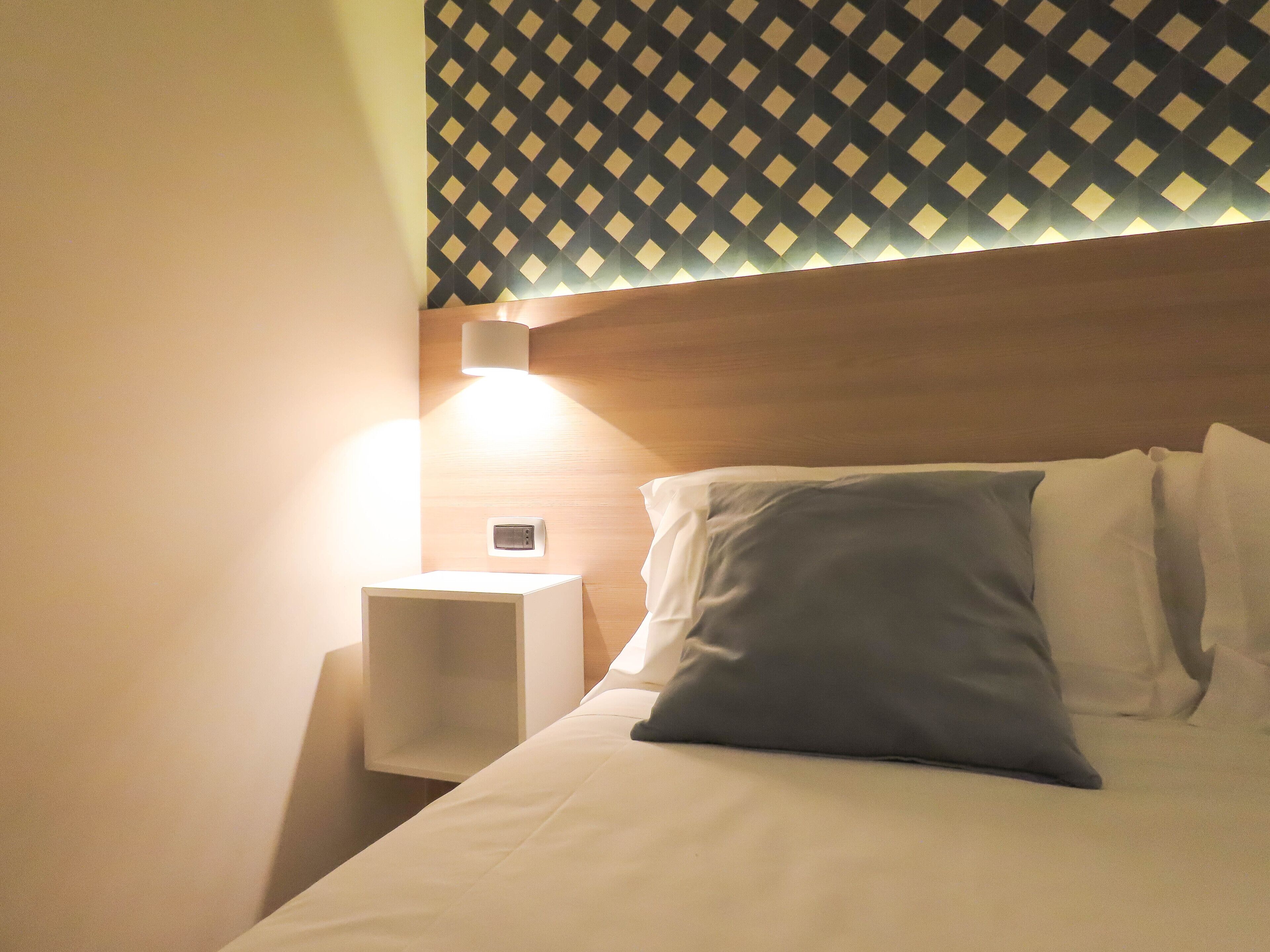 A hotel room with a neatly made bed, a bedside lamp, and a patterned wall.