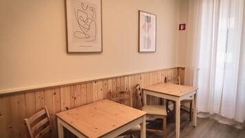 A room with two wooden tables and chairs, a wooden wainscoting, and two framed abstract artworks on the wall.