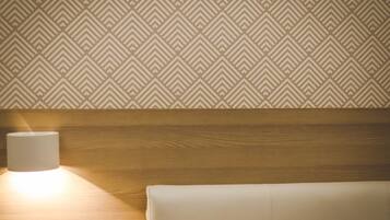 A room with a patterned wallpaper, a wooden headboard, and a bedside lamp.