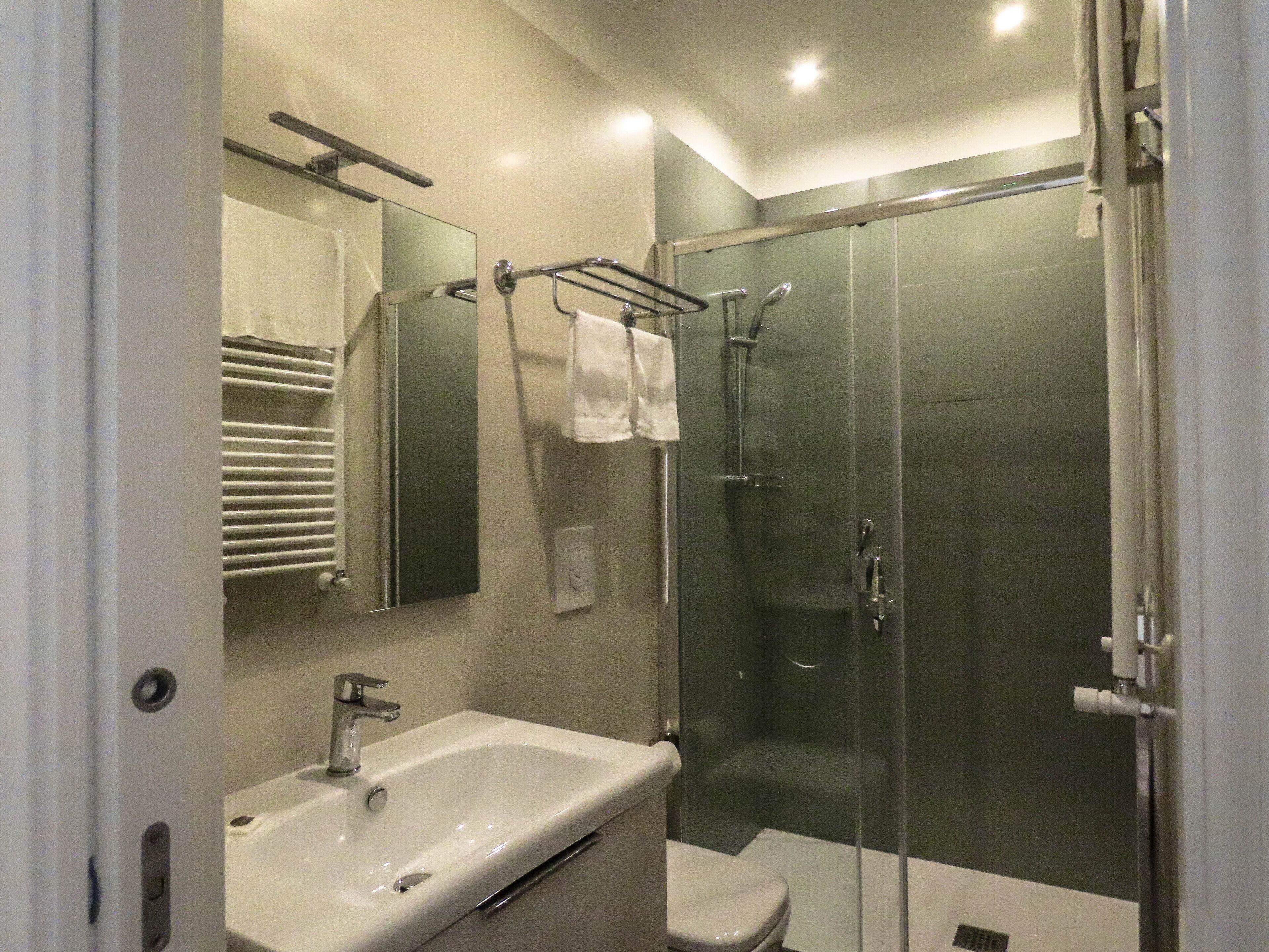 Un baño moderno con ducha envuelta en vidrio, lavamanos blanco y retrete.