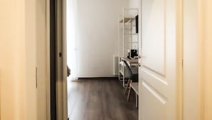 A hallway with a wooden floor, a white door, and a desk with a chair. - My Maison 109 (Rome)