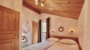 Une chambre avec un plafond en bois, un lit avec une literie blanche, une armoire et un luminaire fixé au mur.