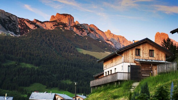 Une maison en bois dotée d’un balcon, entourée d’un paysage montagneux et surplombant un ciel dégagé.