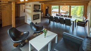 Un salon moderne avec une cheminée, un coin repas avec une grande fenêtre et une cuisine à l’arrière-plan.